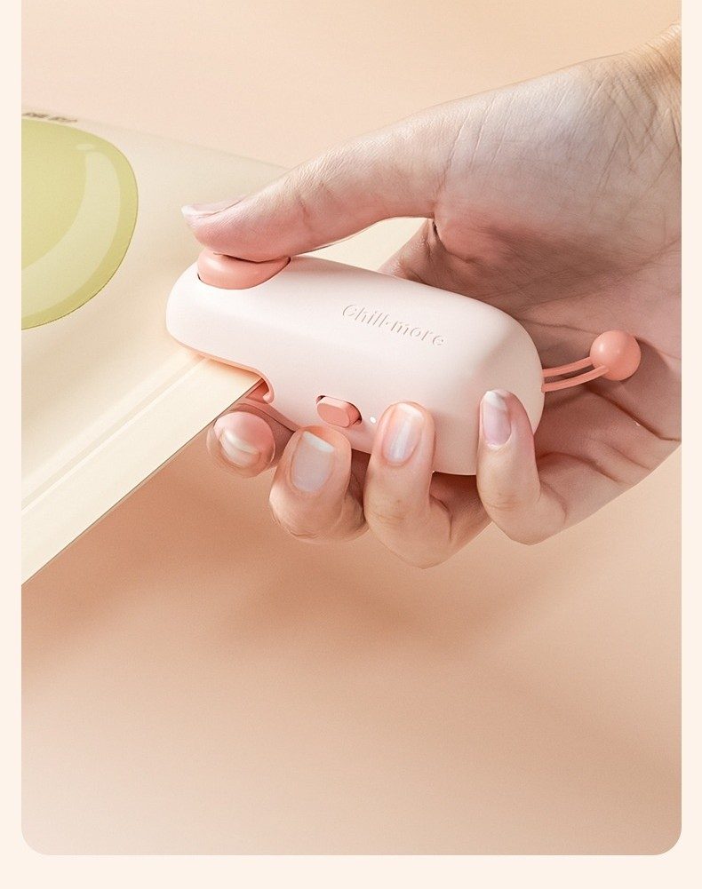 Handheld mini heat sealer sliding along the top of a snack bag (pink pig design)